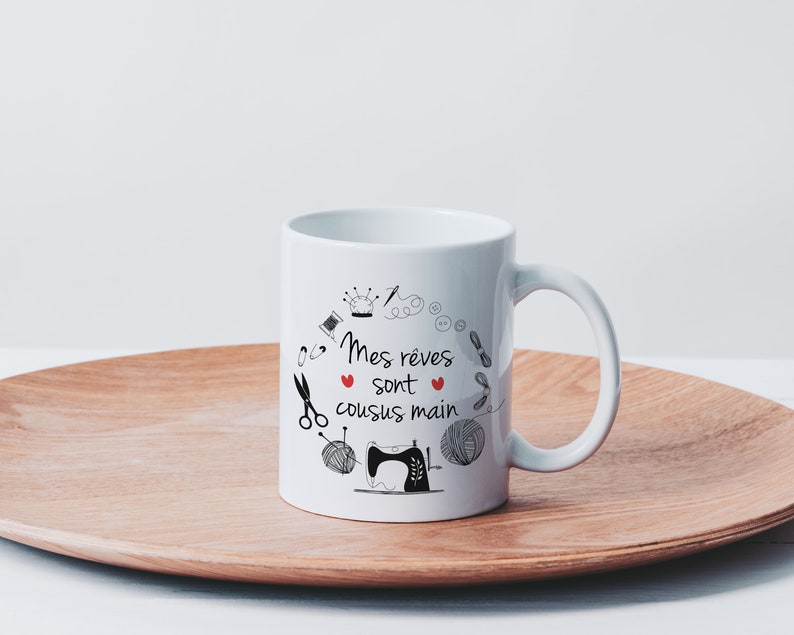 May include: White ceramic mug with a black and white illustration of sewing tools and the text "Mes r&ecirc;ves sont cousus main" with a red heart.