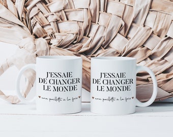 Puede incluir: Dos tazas de cerámica blanca con texto negro que dice "J'ESSAIE DE CHANGER LE MONDE" y "une paillette à la fois".