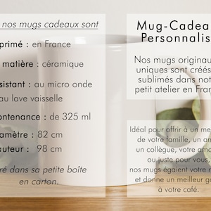 May include: White ceramic mug with black text that reads "Mug-Cadeau Personnalis&eacute;". The mug is 8.2 cm in diameter and 9.8 cm tall. It holds 325 ml. The mug is sitting on a wooden surface with green leaves.