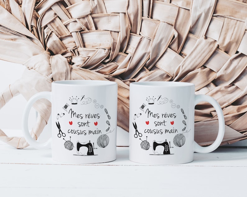 May include: Two white ceramic mugs with black text and illustrations. The text on the mugs reads "Mes reves sont cousus main" which translates to "My dreams are hand-sewn". The mugs feature a sewing machine, yarn, scissors, and other sewing-related imagery.