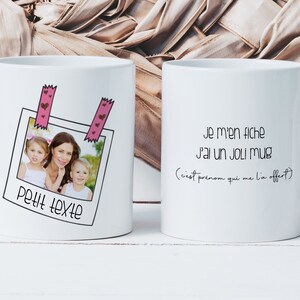 Może przedstawiać: Biały kubek ceramiczny z fotografią matki i jej dwójki dzieci w ramce Polaroid. Kubek ma różową taśmę z sercami i tekst "Petit texte" pod zdjęciem. Druga strona kubka ma tekst "Je m'en fiche J'ai un JOLI Mug (c'est prenom qui me l'a offert)"