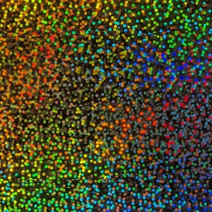 May include: A holographic surface featuring a dense, repeating pattern of small, circular dots. The material displays a vibrant spectrum of iridescent colors, including shifting shades of red, orange, yellow, green, and blue across the texture.