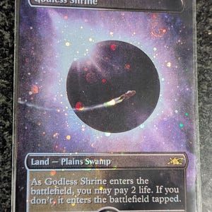May include: A "Godless Shrine" trading card with a cosmic background, a dark planet, and a spaceship. The card is a "Land - Plains Swamp" card. Text on the card includes the card's name, type, and rules text.