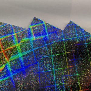 Op de afbeelding: Close-up van iriserend, getextureerd papier met een rasterpatroon. Het papier reflecteert een spectrum aan kleuren, waaronder rood, geel, groen en blauw. De randen van het papier zijn in een driehoekige vorm gesneden.