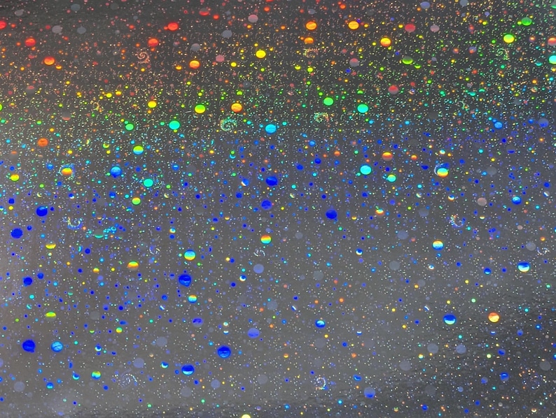 May include: A close-up of a shimmering, iridescent surface with a multitude of colorful, circular specks. The specks range in size and color, including red, orange, yellow, green, blue, and purple, creating a vibrant, speckled effect.