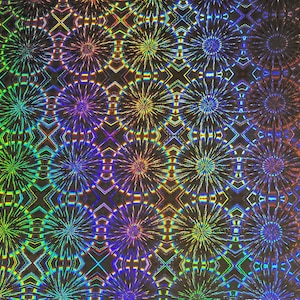 Puede incluir: Una lámina holográfica con un patrón repetitivo de diseños coloridos en forma de estrella. Los colores cambian a través de la superficie, incluyendo rojo, naranja, amarillo, verde, azul y púrpura. El fondo es oscuro, realzando los colores vibrantes.