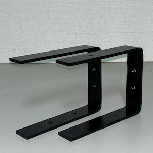 Może przedstawiać: Dwa czarne metalowe wsporniki półki z wieloma otworami montażowymi. Wsporniki mają kształt litery L i płaską powierzchnię na górze.
