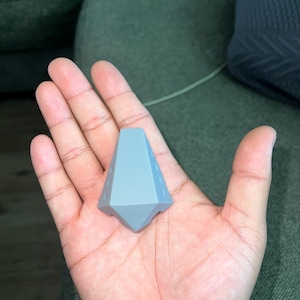 May include: A gray, geometric, 3D printed object with a pointed top and a flat base. The object has a series of small holes around the sides.