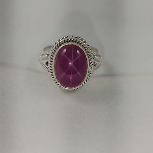 May include: A silver ring with a pink star ruby gemstone set in a twisted rope design.