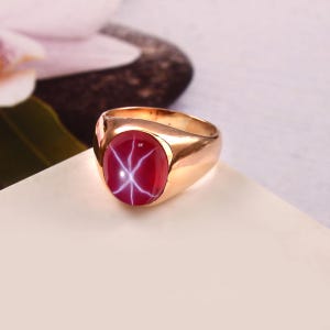 May include: A gold ring with a red star ruby gemstone. The ruby has a star-like pattern inside.