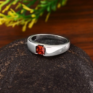 Könnte beinhalten: Ein silberner Ring mit einem quadratischen roten Edelstein.