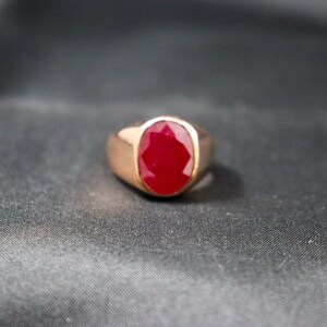 May include: A gold ring with a large, oval-shaped ruby gemstone.