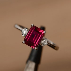 Könnte beinhalten: Ein silberner Ring mit einem großen, smaragdgeschliffenen Rubin und zwei kleineren Diamanten.