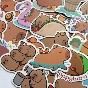 Könnte beinhalten: Eine Sammlung farbenfroher Aufkleber mit Cartoon-Capybaras in verschiedenen Posen. Einige Aufkleber zeigen Capybaras mit Essen, in einem Pool und auf einem Flamingo-Schwimmer. Die Aufkleber haben einen weißen Rand und ein verspieltes, skurriles Design.