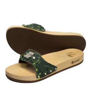 May include: A pair of green and black patterned wooden platform sandals with a buckle closure. The sandals have a brown rubber sole and are made in Italy.