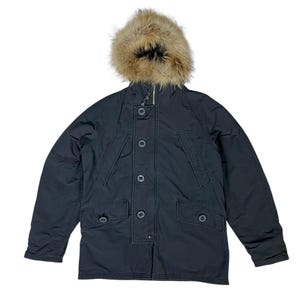 Może przedstawiać: Ciemnoniebieska zimowa parka z kapturem obszytym futrem. Kurtka ma zapinany na guziki przód, dwie kieszenie na piersi i dwie dolne kieszenie. Futrzane wykończenie jest w jasnobrązowym kolorze.