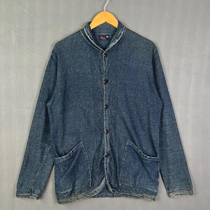 May include: A dark blue denim jacket with a shawl collar, long sleeves, and a button-down front. The jacket features two large patch pockets at the waist and a faded, distressed texture throughout the fabric, hanging on a wooden hanger.
