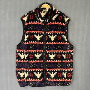 May include: A black fleece vest with a full-length zipper and a high collar. The vest features a repeating pattern of white birds, red flowers, and blue geometric shapes. The vest has two pockets and a black trim.