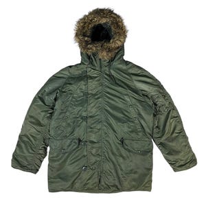 May include: An olive green parka with a fur-trimmed hood. The jacket has multiple pockets, button fastenings, and a zip. The parka is designed for cold weather and has a military-inspired style.