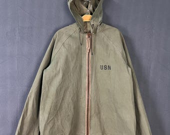 May include: An olive green hooded jacket with a full zipper closure and the letters "USN" printed on the front. The jacket has a drawstring hood and brown accents on the cuffs. The jacket is hanging on a black hanger.