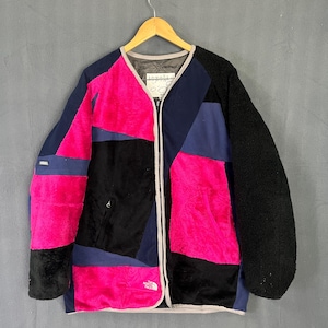 Op de afbeelding: Een patchwork jas met een opvallend kleurenschema. De jas combineert zwarte, marineblauwe en felroze fleece panelen. Voorzien van een volledige ritssluiting en een klein logo.