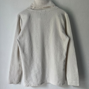 May include: Cream-colored long-sleeved shirt with a textured, vertical striped pattern. The shirt features a wide, folded collar and is hanging on a wooden hanger. The fabric appears to be a medium weight knit.