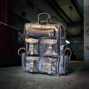 May include: A dark brown leather backpack featuring a top handle, a horizontal zippered pocket, and four lower exterior pockets with flap closures secured by metal buckles. The bag includes two side pockets and visible stitching throughout the design.
