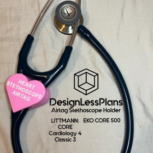 May include: A black stethoscope with a pink heart-shaped AirTag holder attached. The holder has the text "HEART STETHOSCOPE AIRTAG" printed on it. The stethoscope is on a white surface. The text "DesignLessPlans Airtag Stethoscope Holder LITTMANN: EKO CORE 500 CORE Cardiology 4 Classic 3" is printed below the stethoscope.