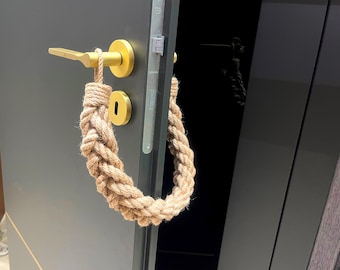 May include: A gold door handle with a rope doorstop. The doorstop is made of natural rope and is wrapped around the handle.