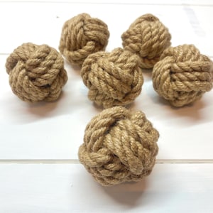 May include: Six natural brown rope balls, each tied in a knot, are arranged on a white wooden surface.