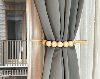 May include: Gray curtain with a wooden beaded tieback. The tieback has a wooden rod with a series of round wooden beads.