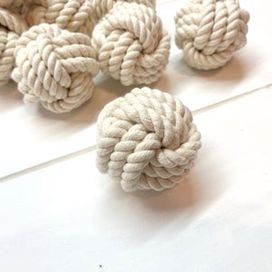 May include: A group of six off-white, knotted rope balls. The balls are made of natural fiber rope and are approximately 2 inches in diameter.