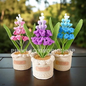 Puede incluir: Tres arreglos florales de ganchillo hechos a mano en macetas beige. Cada maceta tiene un borde festoneado y una pequeña etiqueta que dice "HANDMADE Limited edition". Las flores son rosas, moradas y azules con hojas verdes.
