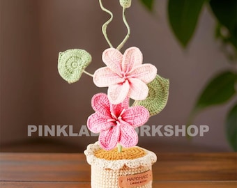 May include: A handmade crochet flower arrangement in a small pot. The arrangement features pink flowers, green leaves, and buds, all crafted with yarn. The pot is beige with a scalloped edge and a "HANDMADE" label.