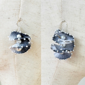 May include: Handmade spiral earrings in shades of grey and white. The edges are trimmed with small white beads, and larger pearlescent beads are set in the centre of each spiral. The earrings are suspended from silver-coloured hooks.