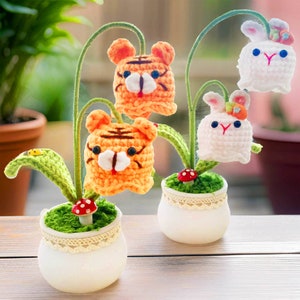 May include: Crochet potted plants with tiger and bunny faces. The orange tigers and white bunnies have embroidered details and are attached to green stems. The white pots have lace trim and a small mushroom.