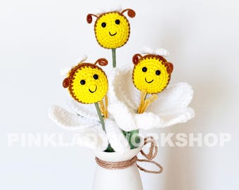 May include: A handmade crochet flower arrangement featuring three smiling yellow bees with brown antennae and accents, nestled in a white flower. The arrangement is in a white vase with a twine accent. The text "PINKLADY WORKSHOP" is visible.