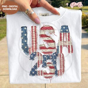 Op de afbeelding: Wit T-shirt met de tekst "USA 250" in een versleten Amerikaans vlagontwerp. De letters zijn gemaakt van rood, wit en blauw textiel, met sterren en strepen. Het shirt heeft een ronde hals en het woord "COMFORT" staat op de kraag.