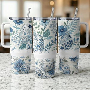 Può includere: Tre bicchieri in acciaio inossidabile con coperchi e cannucce. Ogni bicchiere presenta uno sfondo bianco con un motivo floreale blu e verde con uova.