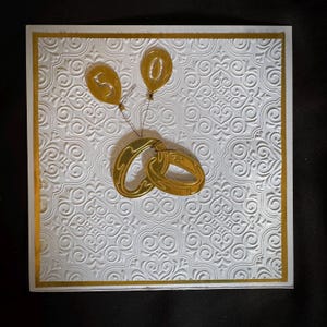 Beautiful Gold Wedding Rings For Anniversary Or Wedding Greeting Card On An Embossed White Background.