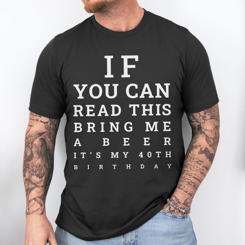 May include: A black short-sleeved crew neck t-shirt featuring white text that reads: IF YOU CAN READ THIS BRING ME A BEER IT'S MY 40TH BIRTHDAY. The lettering is arranged in a block style, mimicking an eye chart, centered on the chest area.