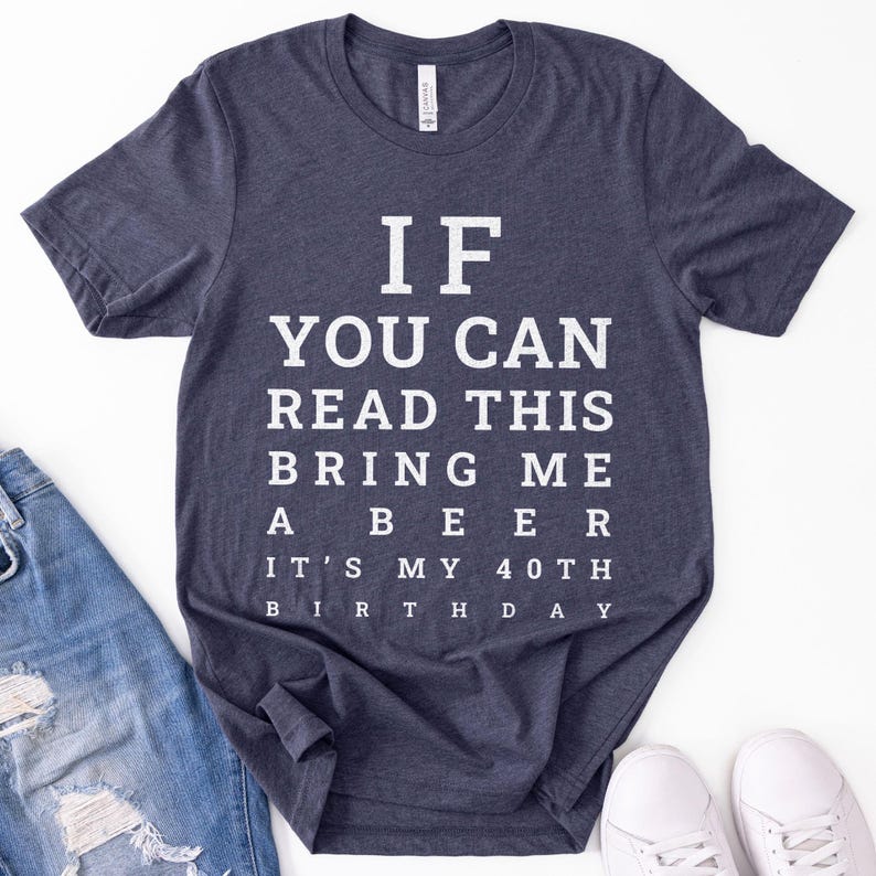 May include: A dark heather navy blue short-sleeve t-shirt featuring white text printed in an eye chart style that reads: IF YOU CAN READ THIS BRING ME A BEER IT'S MY 40TH BIRTHDAY. The shirt has a crew neckline and a standard fit design.