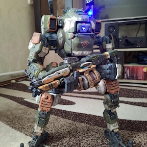 May include: A detailed model of a military-style robot, featuring a color scheme of green, brown, and orange. The robot has multiple weapons and a complex mechanical design. It stands on two legs and has two missile launchers on its shoulders.