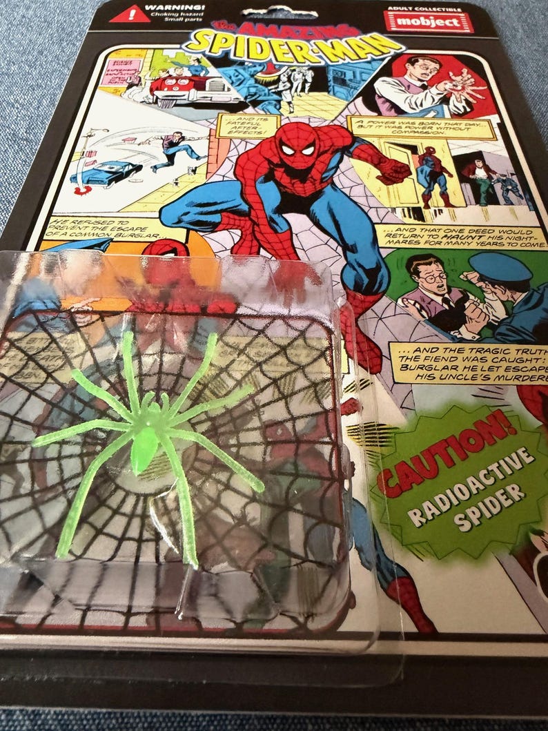 Pu&ograve; includere: Una action figure di Spider-Man in una confezione di plastica trasparente, con un giocattolo a forma di ragno radioattivo verde. La confezione presenta illustrazioni di fumetti e le parole "The Amazing Spider-Man" e "Caution! Radioactive Spider."