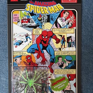 Pu&ograve; includere: Una action figure in stile vintage di The Amazing Spider-Man, confezionata su una scheda a tema fumetto retr&ograve;. La scheda presenta pannelli di fumetti e un giocattolo a forma di ragno radioattivo verde. La confezione include il testo "WARNING! Choking hazard Small parts".