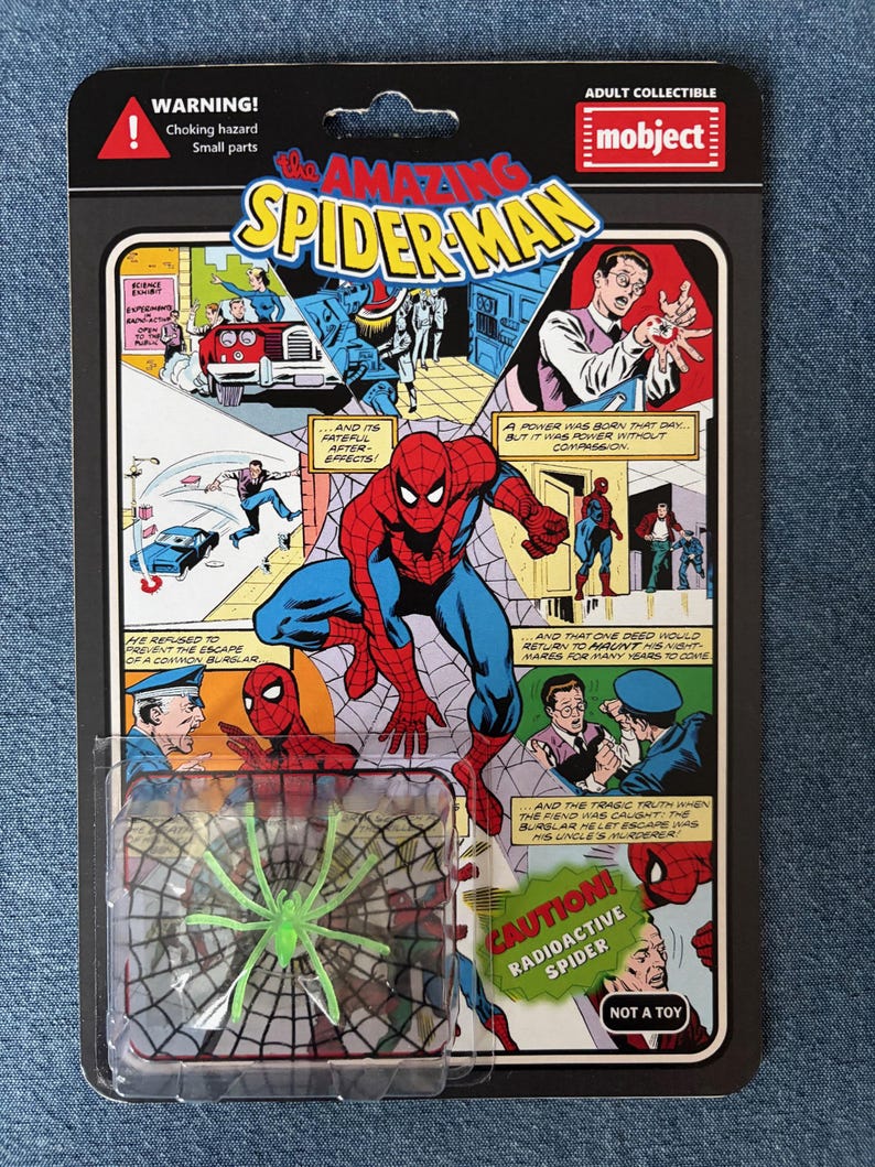 Pu&ograve; includere: Una action figure in stile vintage di The Amazing Spider-Man, confezionata su una scheda a tema fumetto retr&ograve;. La scheda presenta pannelli di fumetti e un giocattolo a forma di ragno radioattivo verde. La confezione include il testo "WARNING! Choking hazard Small parts".