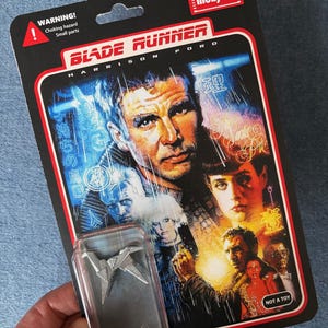 May include: A "Blade Runner" collectible action figure, featuring Harrison Ford, on a black card with the film title and warning labels. Includes a small, silver origami figure in a clear plastic case.