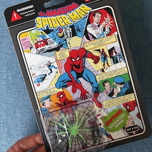 Pu&ograve; includere: Action figure da collezione di Spider-Man per adulti in una confezione retr&ograve;. La confezione presenta fumetti con illustrazioni di Spider-Man e il testo "The Amazing Spider-Man". Un blister trasparente contiene un giocattolo a forma di ragno radioattivo verde.