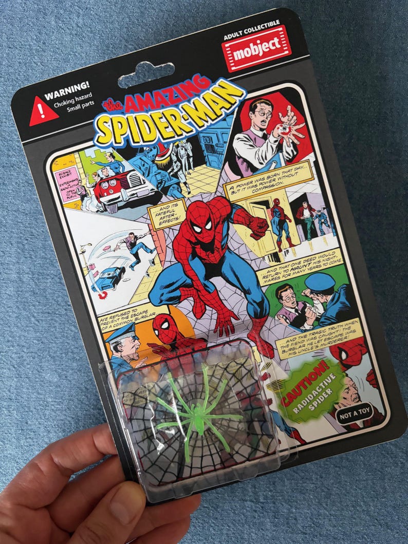 Pu&ograve; includere: Action figure da collezione di Spider-Man per adulti in una confezione retr&ograve;. La confezione presenta fumetti con illustrazioni di Spider-Man e il testo "The Amazing Spider-Man". Un blister trasparente contiene un giocattolo a forma di ragno radioattivo verde.