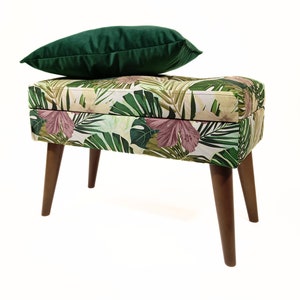 May include: A green velvet cushion sits atop a storage bench with a tropical leaf print. The bench has four wooden legs.